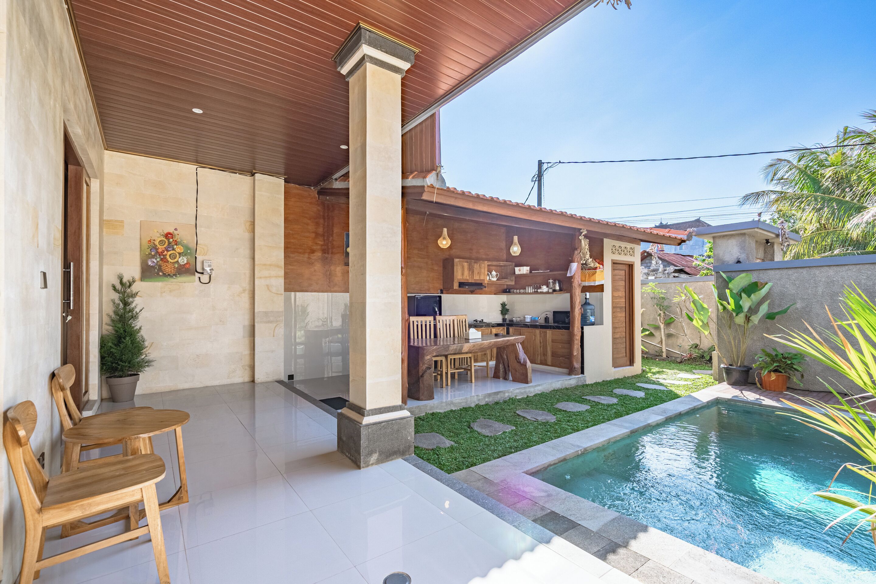A modern outdoor living area with a pool, wooden furniture, and a kitchen.