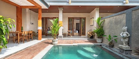 Zona de piscina con terraza de madera, plantas en macetas y una estatua.