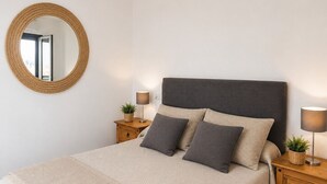 Een slaapkamer met een bed, twee nachtkastjes, een ronde spiegel en twee wandlampen.