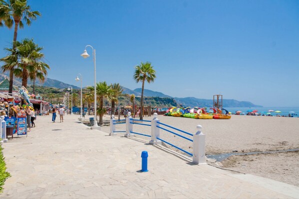 A beachside promenade with palm trees, a blue railing, and beach umbrellas.