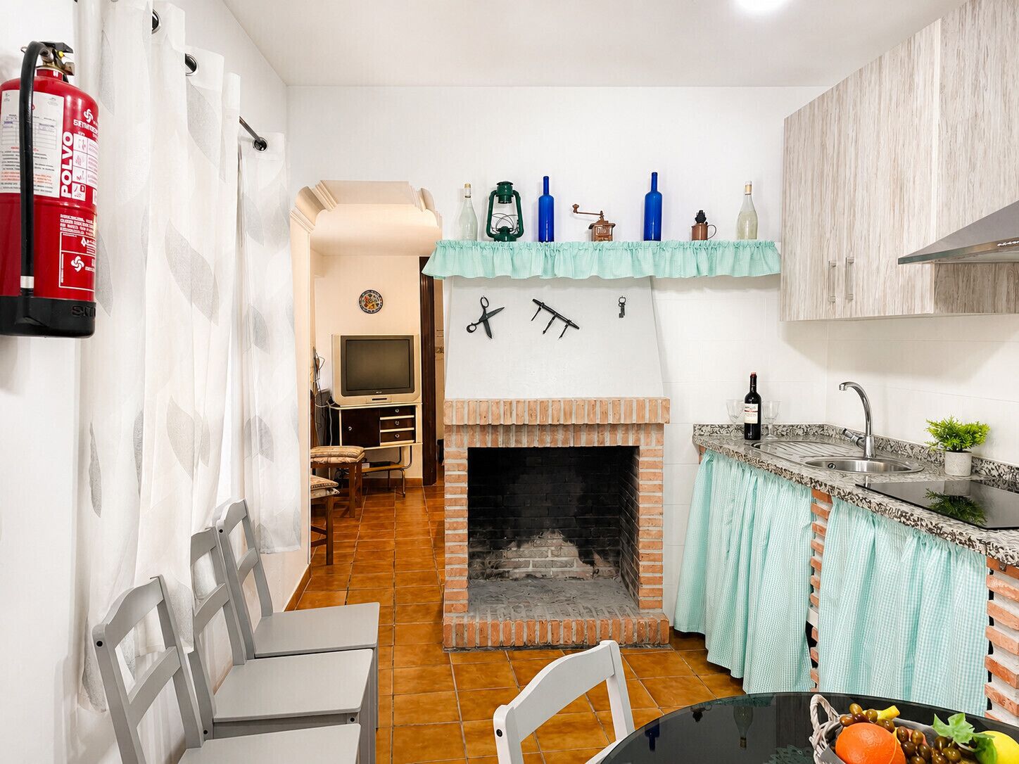 A kitchen with a fireplace, a dining area with chairs, a TV, and a fire extinguisher.