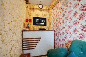 A hotel reception area with a reception desk, a clock on the wall, and a sign indicating the hotel name and service type.