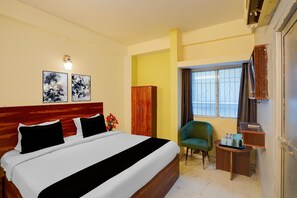 A hotel room with a bed, a wooden wardrobe, a green armchair, a small table with a remote control, and a window with curtains. - Classic Hotel Newyork (Patna)