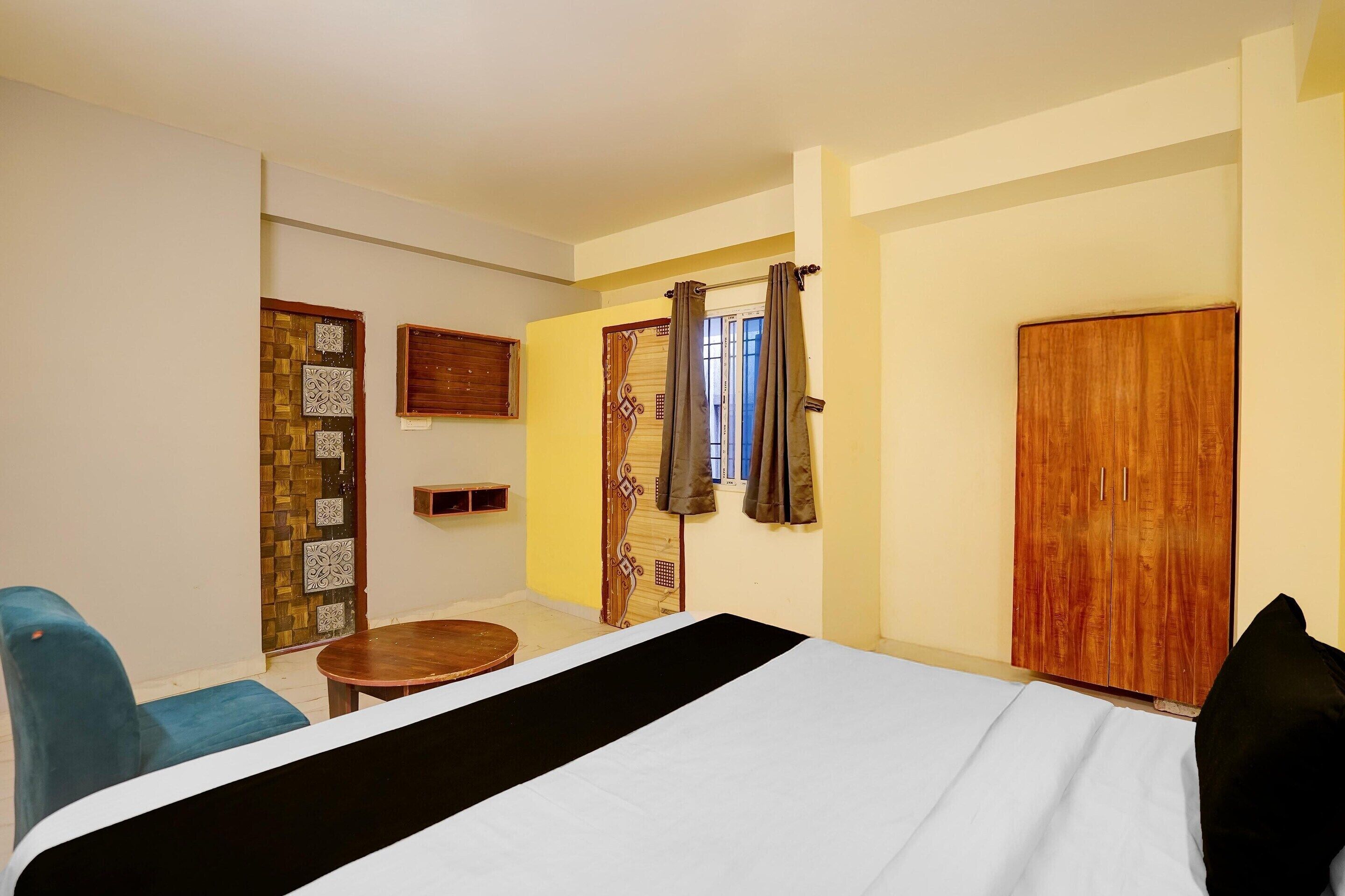 A hotel room with a bed, a small table, a chair, a wardrobe, and a door with decorative panels.