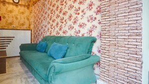 En turkosfärgad soffa med blå kuddar i ett rum med blommigt tapetmönster och en vägg med tegelstensmönster.