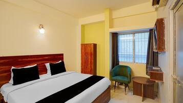 Une chambre d’hôtel avec un lit, une chaise, une petite table, une armoire et une fenêtre avec des rideaux.
