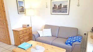 Een kamer met een houten tafel, een bank, een kapstok en twee afbeeldingen in lijsten aan de muur.