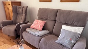 Ein Wohnzimmer mit grauem Sofa, einem Holztisch und einer Vase mit getrockneten Blumen.