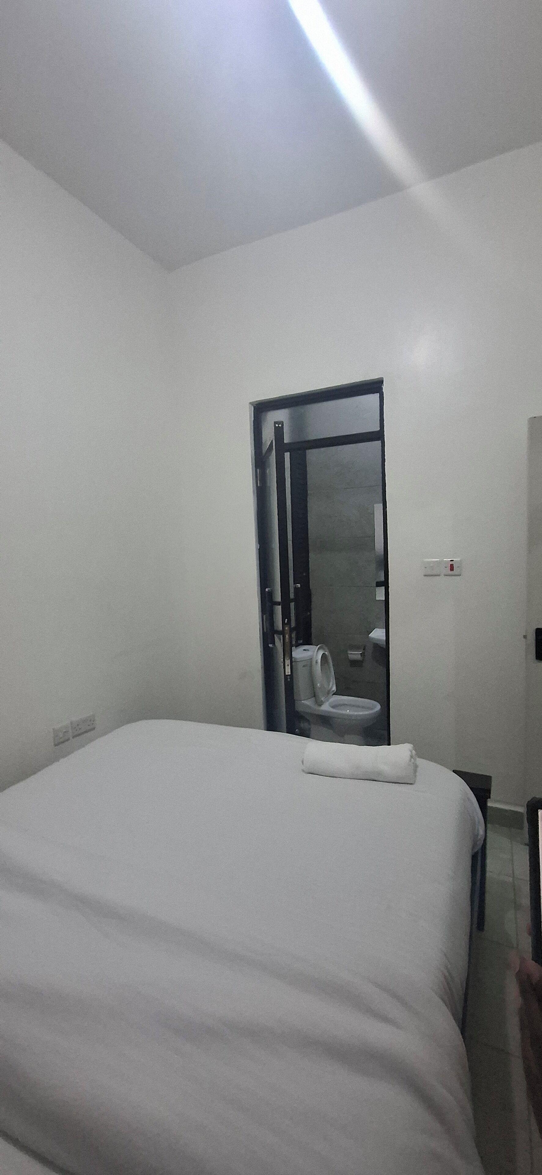 Une chambre d’hôtel avec un grand lit, une porte donnant sur une salle de bain et un luminaire au plafond.
