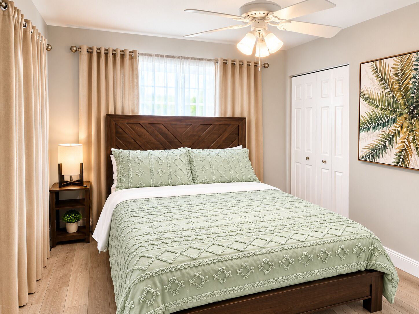 Een slaapkamer met een houten hoofdbord, een bed met een groene deken, een nachtkastje met een lamp en een plafondventilator.