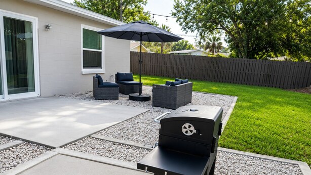 Eine Hinterhofterrasse mit Grill, Gartenmöbeln und einem Holzzaun.
