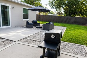 Eine Hinterhofterrasse mit Grill, Gartenmöbeln und einem Holzzaun.
