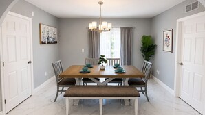 Ein Esszimmer mit Holztisch, sechs Stühlen, einer Bank, einer Chandelier und einer Topfpflanze.