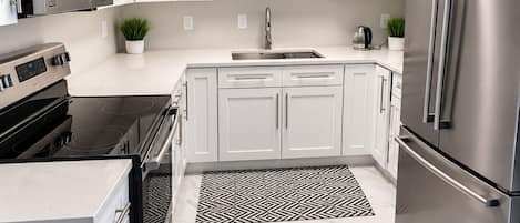 A modern kitchen with white cabinets, stainless steel appliances, and a marble floor.