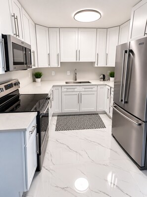 A modern kitchen with white cabinets, stainless steel appliances, and a marble floor. - 4-bedroom house in perfect Cocoa with cool AC for relaxing stays (Cocoa)