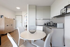 A modern kitchen with white cabinets, a microwave, and a kettle. There is a dining area with a round table and white chairs. - Apartment 'La Casa Di Luca' with Shared Pool, Wi-Fi and Air Conditioning (Sirmione)