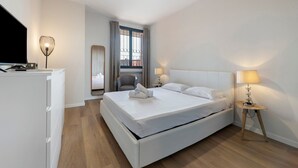 A hotel room with a bed, a desk, a chair, a TV, a ceiling fan, and a window with curtains.