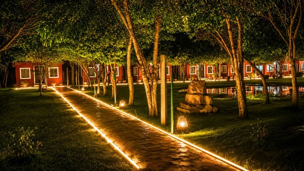 A pathway lined with trees leading to a row of red buildings with windows.
