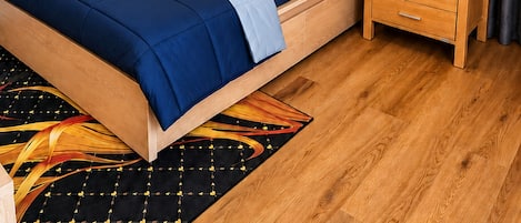 A bedroom with a bed, bedside table, lamp, ceiling fan, and artwork on the wall.