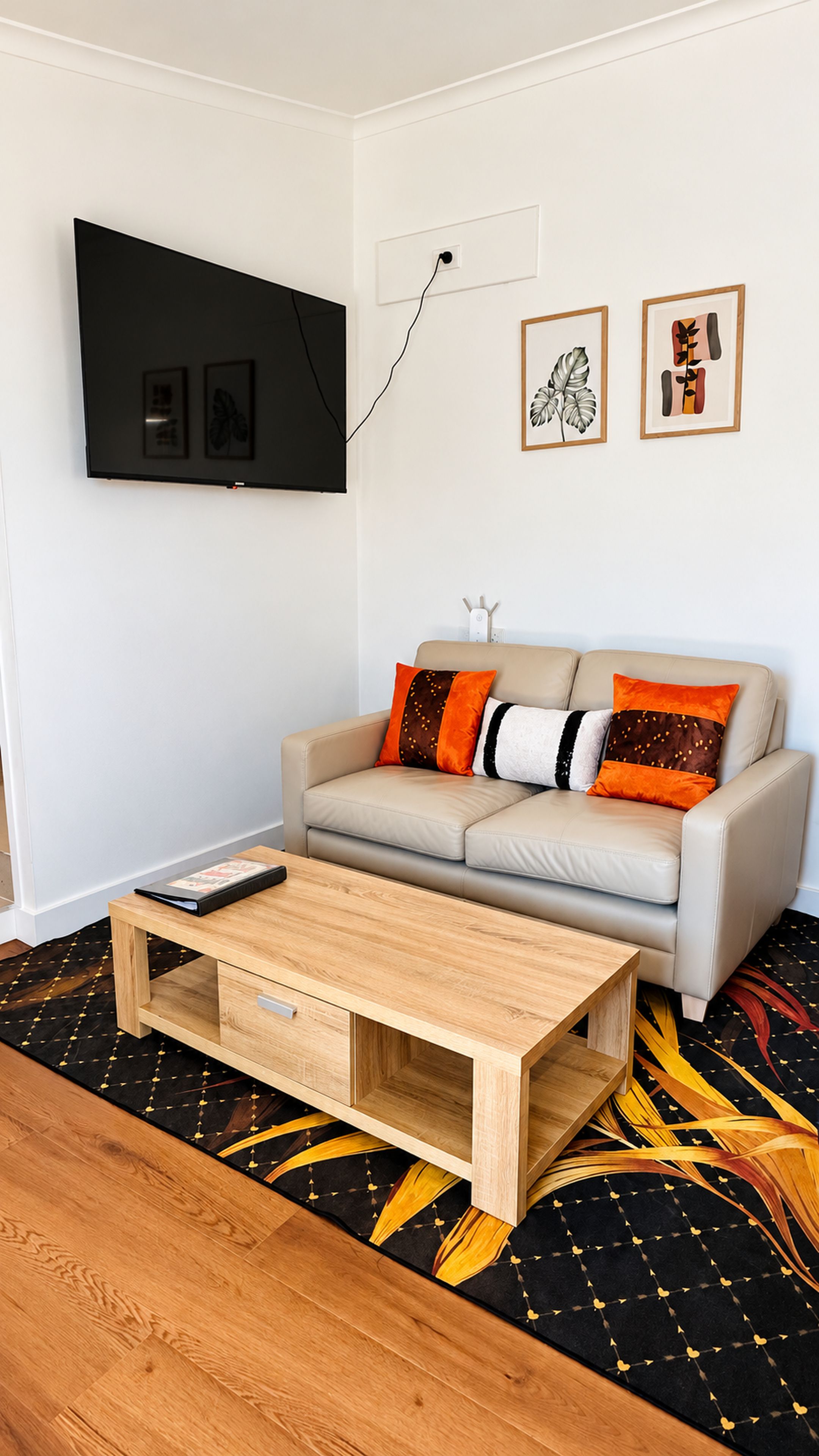 Ein Wohnzimmer mit einer Couch, einem Couchtisch, einem an der Wand befestigten Flachbildfernseher und zwei gerahmten Kunstwerken.