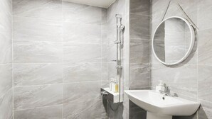 Une salle de bain avec des carreaux gris, une douche, un lavabo et un miroir rond.