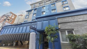 Un bâtiment d’hôtel avec une enseigne bien visible indiquant « HÔTEL », un espace de stationnement et une entrée fermée par un portail.