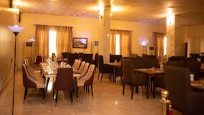A restaurant with a long table set for dining, multiple chairs, and a television on the wall. - Luziana Hotels (Abuja)