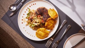 A plate of food with a steak, coleslaw, and fried plantains on a white plate. - Luziana Hotels (Abuja)
