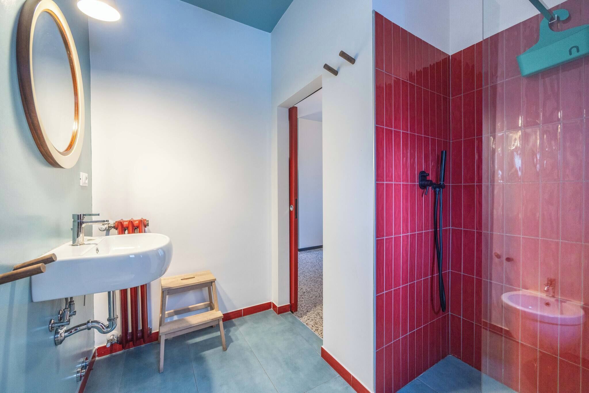 A bathroom with a sink, mirror, shower, and red-tiled walls.
