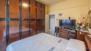 Ett hotellrum med en säng, en TV, ett skrivbord med en stol, en garderob och en dörr som leder till ett badrum.
