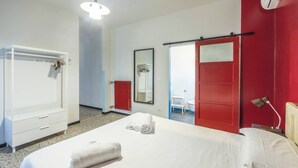 Ein Hotelzimmer mit Bett, Kleiderschrank, Spiegel, einer roten Tür und einem durchgehenden Türspalt einsehbaren Badezimmer.