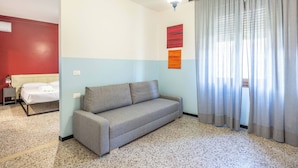 Ein Zimmer mit einer Couch, einem Bett, einer Wand-Klimaanlage und einem mit Vorhängen versehenen Fenster.