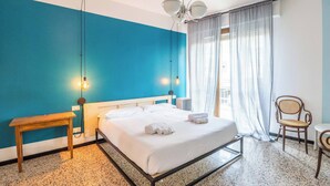 Un dormitorio con cama, mesita de noche, una silla y una ventana con cortinas.