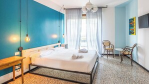 Una habitación de hotel con cama, escritorio, silla, televisor y ventana con cortinas.