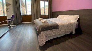 Ein Schlafzimmer mit Bett, Schreibtisch und großen Fenstern.