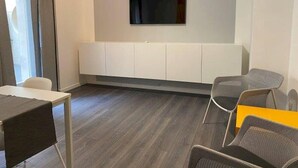 Ein modernes Zimmer mit einem flachbildfernseher an der Wand, einem weißen Schrank darunter und einem grauen Sessel.