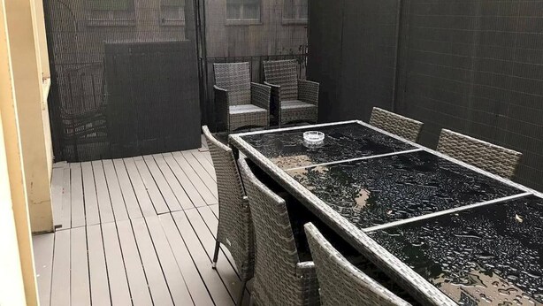 Eine Außenpatio mit Tisch und Stühlen, einem Zaun und einem Gebäude im Hintergrund.