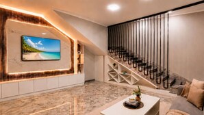 Un salon moderne doté d’un grand téléviseur, d’un sol en marbre, d’un escalier et d’un coin salon confortable.
