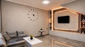 Un salon moderne comprenant un canapé, une table basse, une horloge murale, un téléviseur et une étagère décorative.