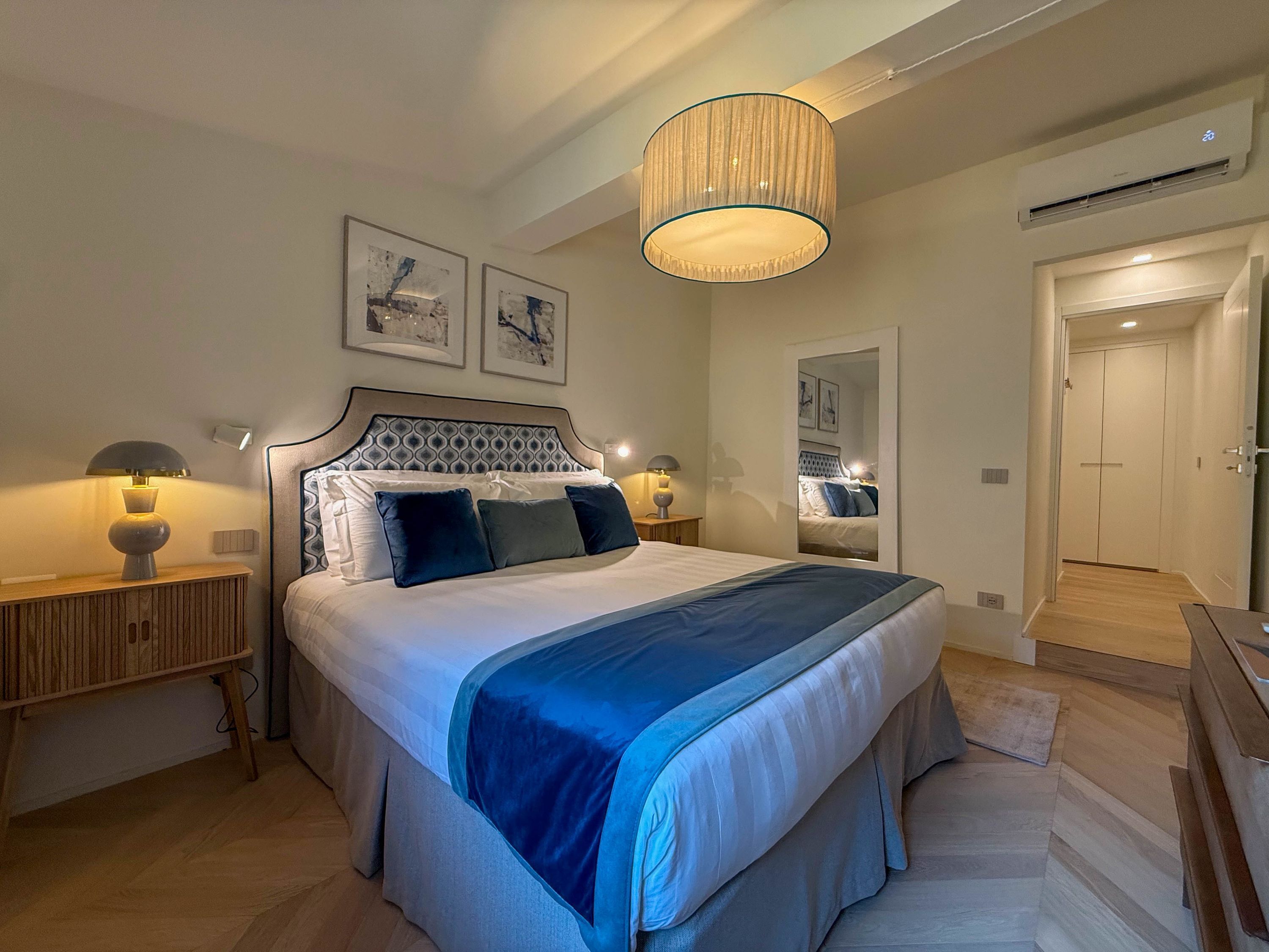 Une chambre à coucher avec un lit, des lampes de chevet, un miroir et un luminaire au plafond.