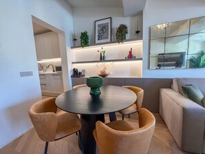 Ein moderner Essbereich mit einem runden Tisch, vier Stühlen, einer Couch und einer Küche im Hintergrund.