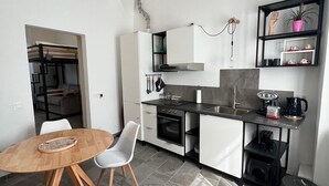 Eine kompakte Küche mit Esstisch, weißen Schränken, einem Einbauofen und einer kleinen Kaffeestation.