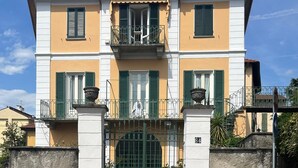 Ein zweistöckiges Gebäude mit geschlossenem Eingang, einem Balkon mit schmiedeeisernem Geländer und einer Steinmauer.