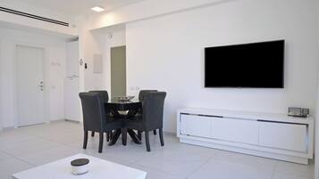 Un salon moderne comprenant une table à manger, des chaises, un téléviseur et un meuble blanc.