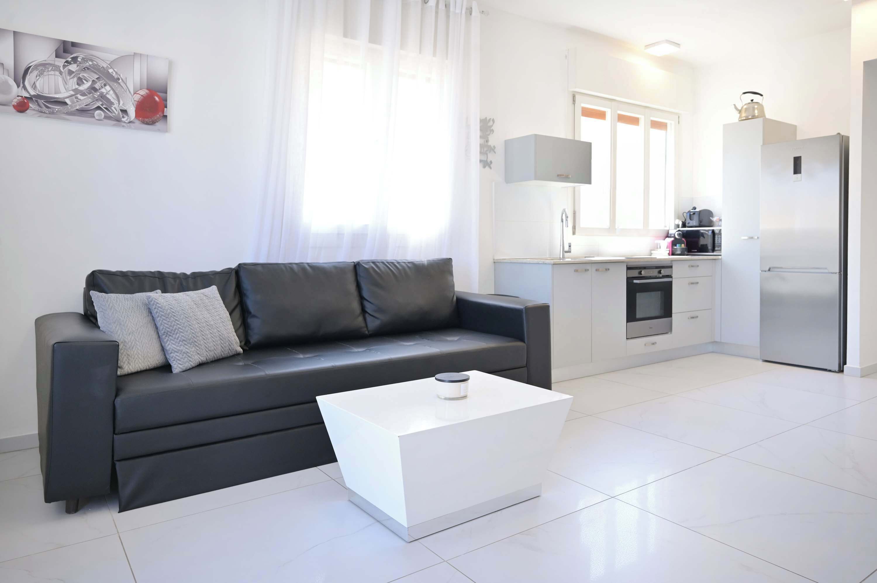 Un salon moderne comprenant un canapé, une table basse, un coin cuisine avec un réfrigérateur et une fenêtre avec des rideaux.