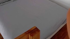 Una habitación con una cama, cabecera de madera y pared blanca con interruptor de luz.