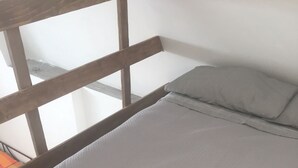 Una cama con colchón gris y almohadas blancas, cabecera de madera y una toalla blanca doblada sobre la cama.