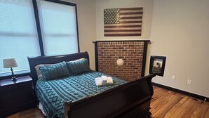 Ein Schlafzimmer mit einem Bett, einem Deckenventilator, einem Kamin aus Backstein und einer amerikanischen Flagge.