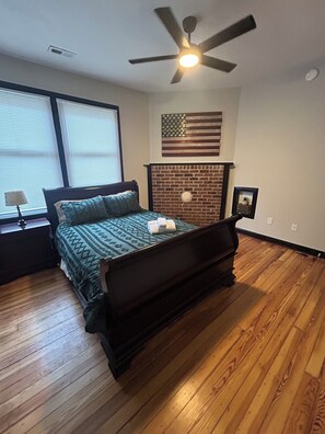 Ein Schlafzimmer mit einem Bett, einem Deckenventilator, einem Kamin aus Backstein und einer amerikanischen Flagge.