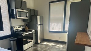 Eine moderne Küche mit Edelstahlgeräten, einer Mikrowelle, einem Backofen und einem Kühlschrank, Holzboden und einem Fenster mit Jalousien.